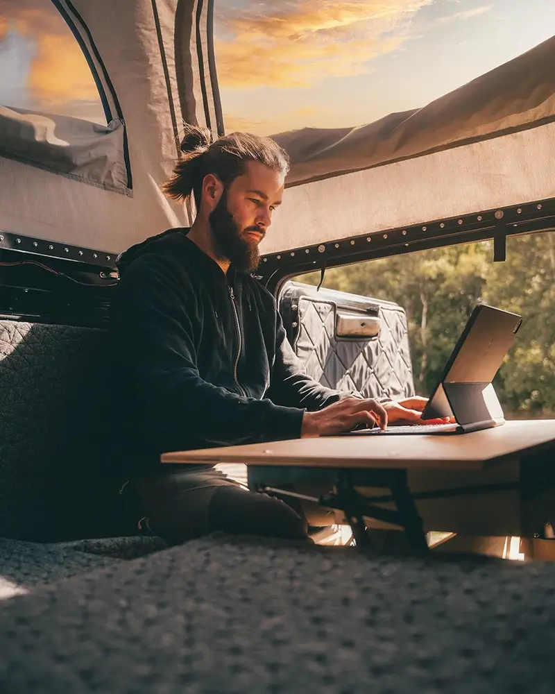 Junger Mann arbeitet an seinem Laptop, sitzend auf einer Vanmade Matratze