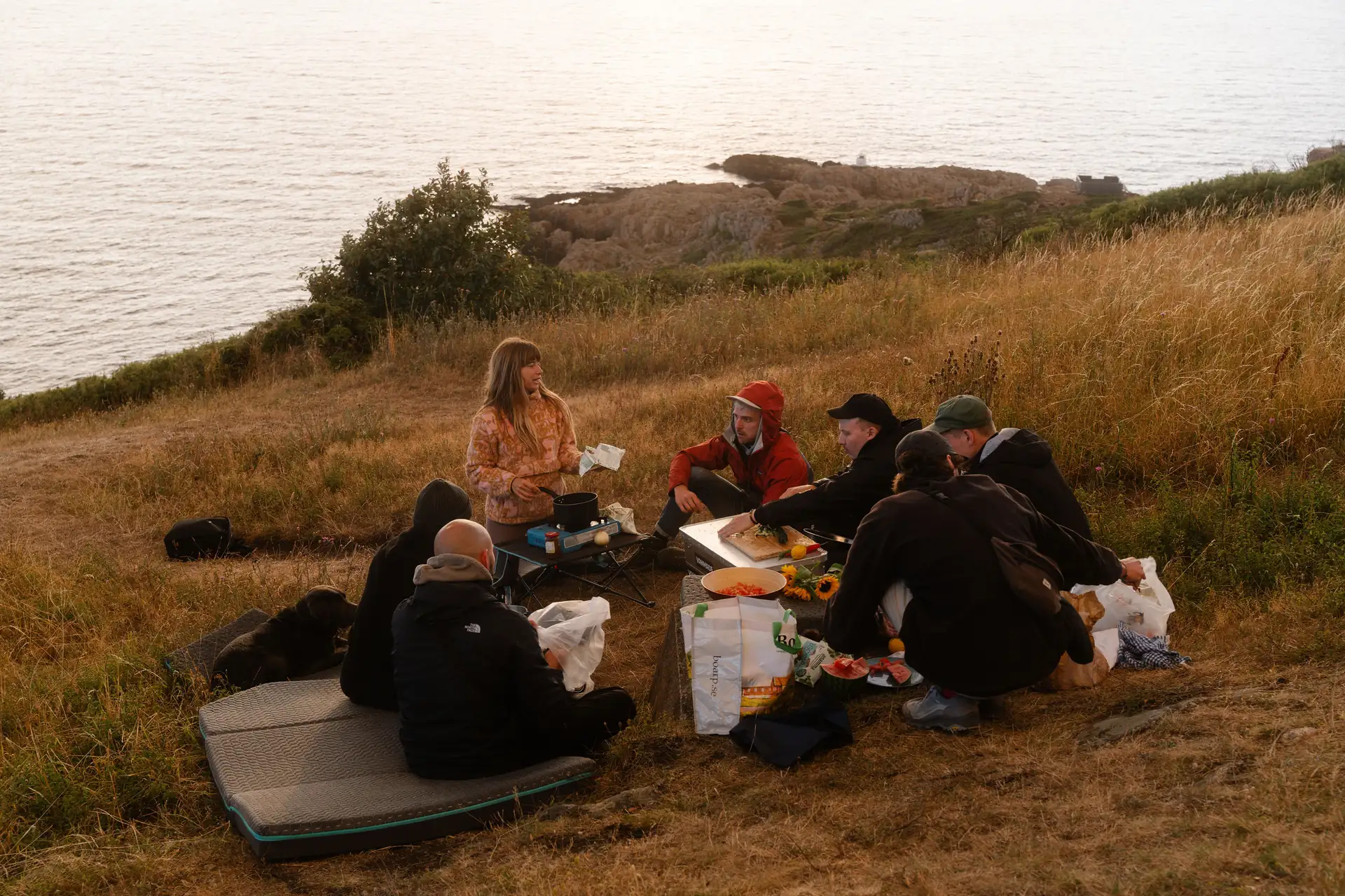 Lifestyle, Freunde sitzen auf Vanmade Matratze auf einer Wiese an der Kueste, picknick, Abendstimmung
